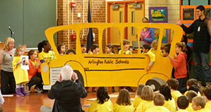 Children onstage in a play with a cardboard bus cutout.