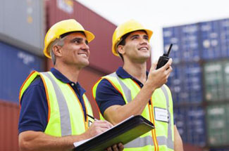 A photograph of two people working at a port.