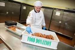 Chef placing cooked bacon into commercial kitchen sorting bin marked "Food Donations".