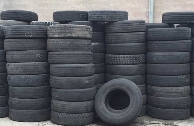 This is a picture of black rubber tires. There are more than a handful of stacks of whole tires, which are at least eight tires high.