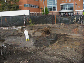 The former Lawrence Metals site in the city of Chelsea, Massachusetts, is a 1.8-acre property close to a hotel, Chelsea High School, and a community swimming pool. In this picture, a man in all-white gear is standing on soil in an enclosed area.