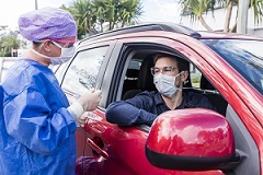 Man giving a hospital worker a test swab while sitting in a car