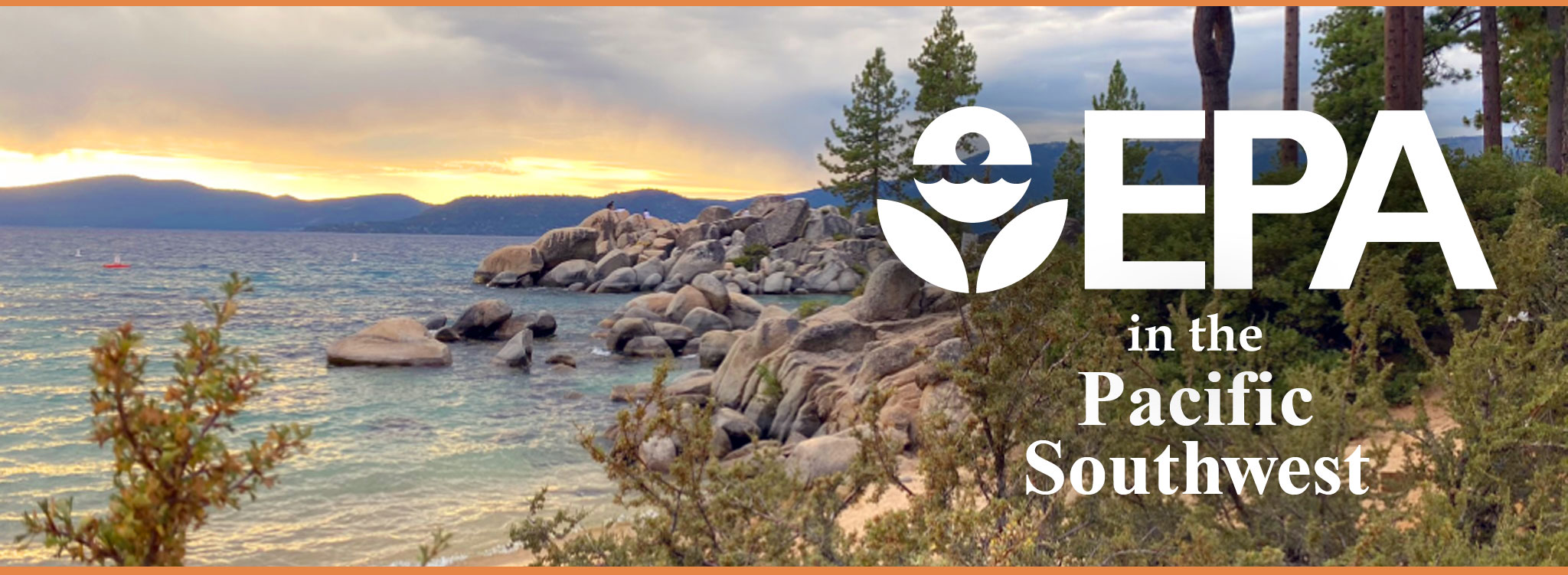 View of sandy beach shoreline with pine trees and large boulders