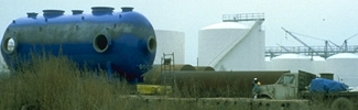 A large blue aboveground storage tank on a grassy field at an industrial facility