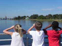 Three kids looking over a body of water with binoculars