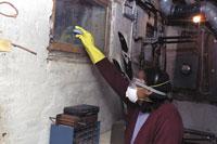 Person cleaning mold while wearing protective equipment