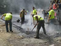 The pavement crew spreads a section of asphalt with shovels.