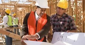 Two workers consulting blue prints while standing inside the frame of a new house.