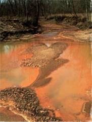 Photo of a stream discolored (orange) from dust and sediment from mining.
