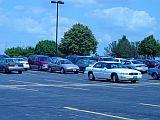 Photo showing a parking lot with parked cars and a few trees in the distance.