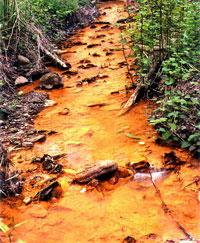 Photo shows a stream entirely colored metallic orange from acid mine runoff.