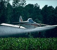 Photo of a crop duster airplane spraying agricultural fields with pesticides.