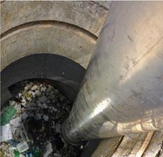 View down a Hydrodynamic Separator: cylindrical concrete catchment with trash at the bottom.