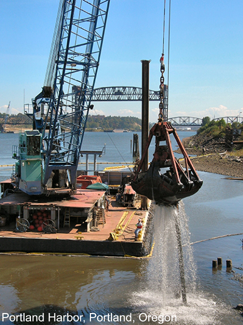 A photograph of a crane on a barge dredging a water channel.
