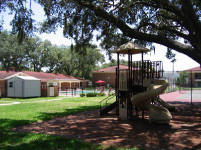 Shaded playground area on the Site with pool and leasing office buildings in the background
