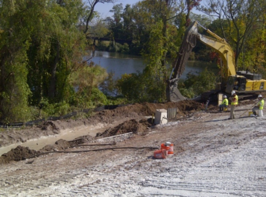 A photograph of an excavator digging a trench, with workers observing nearby.