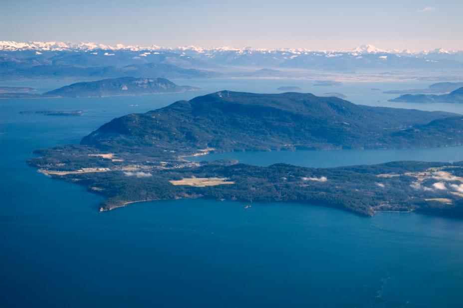 Deep blue water and lush dark green islands arise from it. In the distance the white caps of the mountains are seen among mist