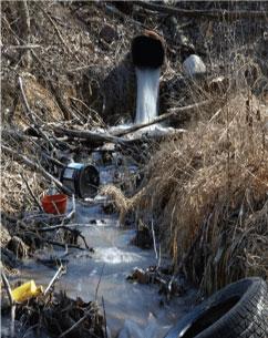 Drainage pipe emptying into a stream with plastic garbage in the channel.