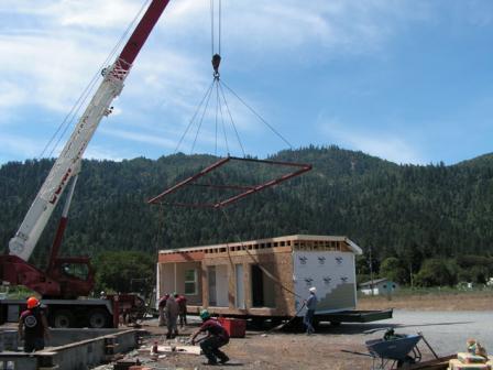 Manufactured home being lifted off of a flatbed with a crane for installation on site.