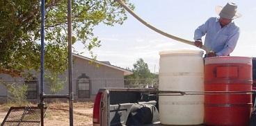 Man filling up water drums at water hauling station in Ganado