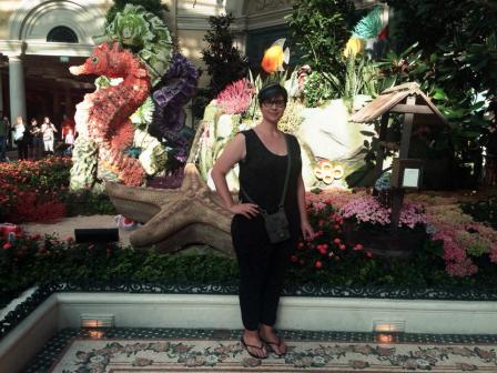Angela Batt stands in front of a garden and sculptures of sea horses