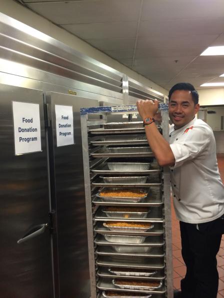 This is a picture of a kitchen worker standing next to a cart of food donations