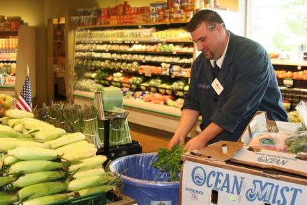 This is a picture of a Big Y Markets employee in the produce section placing organic waste in a blue barrel.