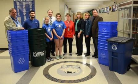 This is a picture of nine people standing around numerous recycling and composting bins.