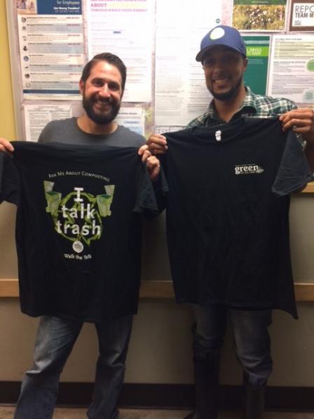 This is a picture of two Whole Foods employees holding up shirts that say I talk trash, Ask me about composting and walk the talk.