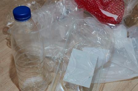 This is a picture of different types of plastics on a table, including a bottle, a bag, different wraps, and packaging.