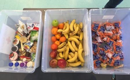 This is a picture of three clear bins filled with fruit, vegetables, yogurt, milk and other extra food. 