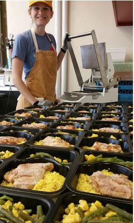 This is a picture of a kitchen worker filling containers of meals to be donated.