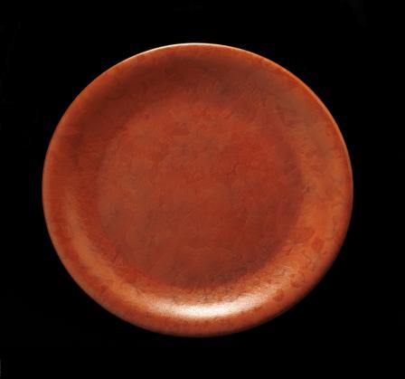 This is a picture of a red-orange plate, created by Glen Lukens, which is covered in a ceramic glaze that contains uranium. Uranium gives the plate its color, but also emits small amounts of radiation.