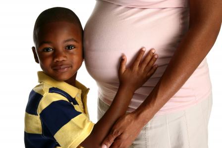 A young boy presses his ear against the pregnant belly of his mom