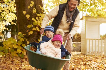 Father pushing kids on a wheelbarrow on fall leaves.