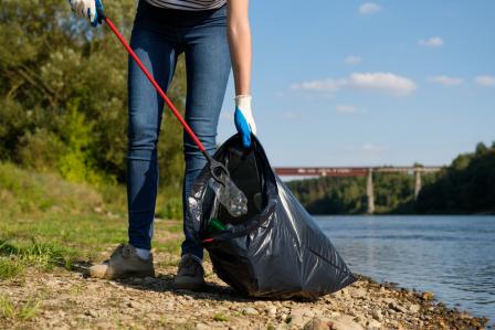 Picture of a volunteer picking up plastic litter on the coast of a river clean-up project.
