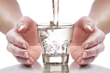Hands are cupped around a clear drinking glass filling with water