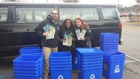 This is a picture of three students from University of Albany standing next to numerous blue recycling bins.