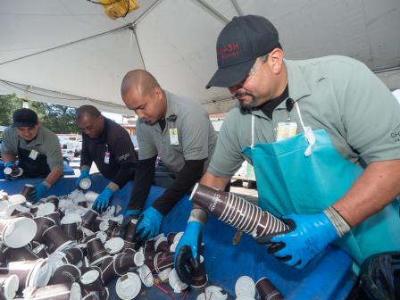 This is picture of men putting cups into a recycling bin