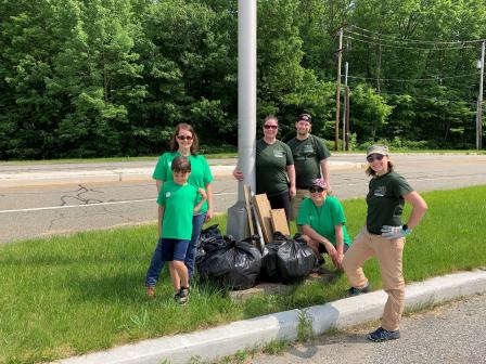 This is a picture of group of people in green shirts cleaning up the side of a road.
