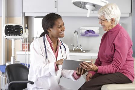 A female doctor speaks with an elderly patient while holding a tablet