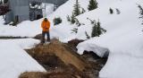 Researcher in an orange coat takes a soil sample at a former mining site