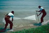 Two men wearing waders are standing in one of the Great Lakes with a net stretched between them that they are dragging in the water.