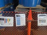 Closeup view of signs posted on fencing surrounding drums containing stored batteries.
